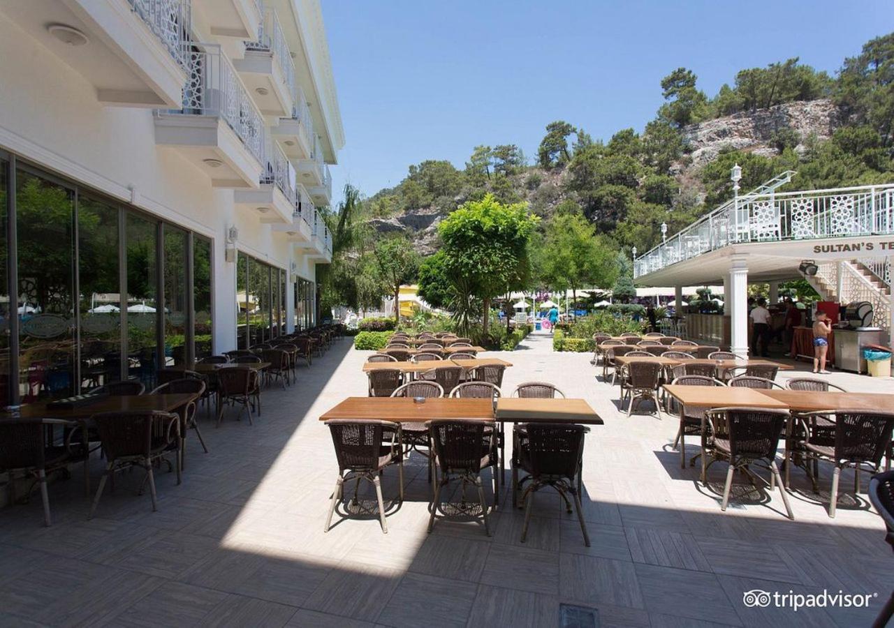 Miramor Hotel & Spa Antalya Ngoại thất bức ảnh The photo shows an outdoor dining area, likely at a restaurant or cafe. There are several tables with chairs arranged neatly on the paved ground, and some greenery, such as trees and plants, is visible in the background. The setting appears bright an